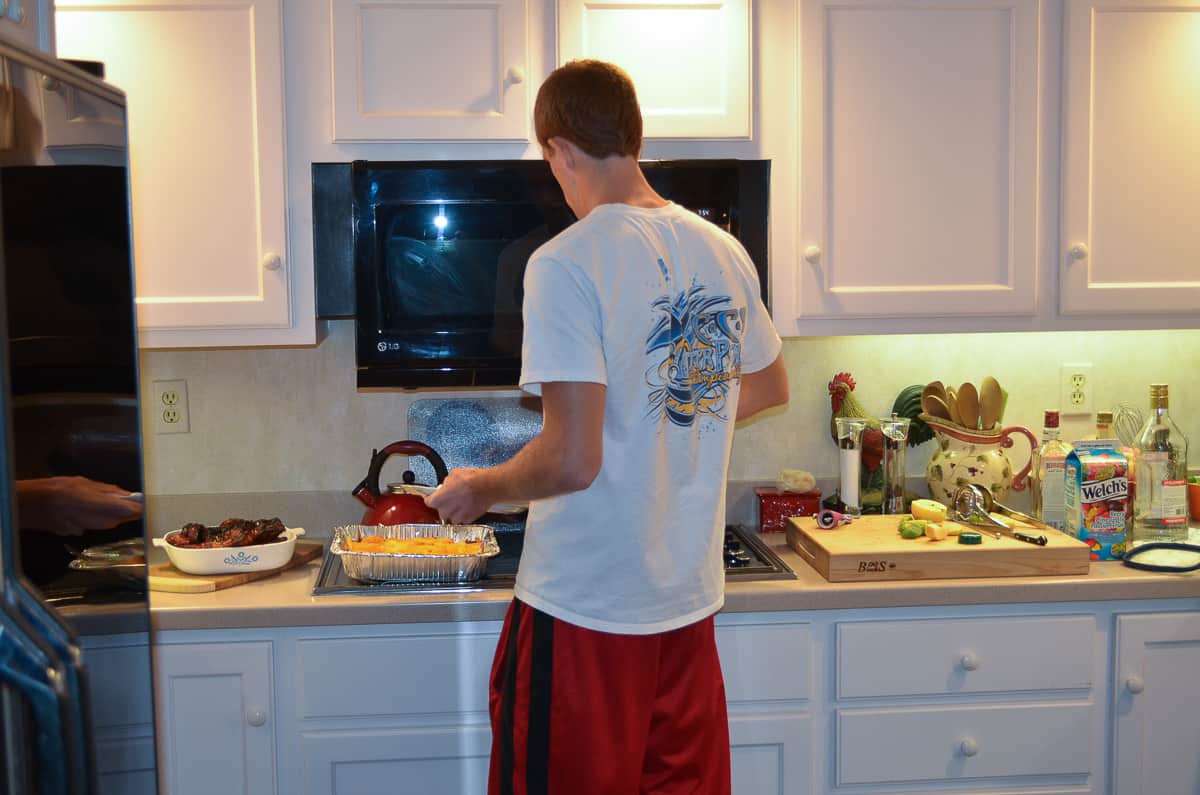 A young man in a kitchen putting food on to his dinner plate.