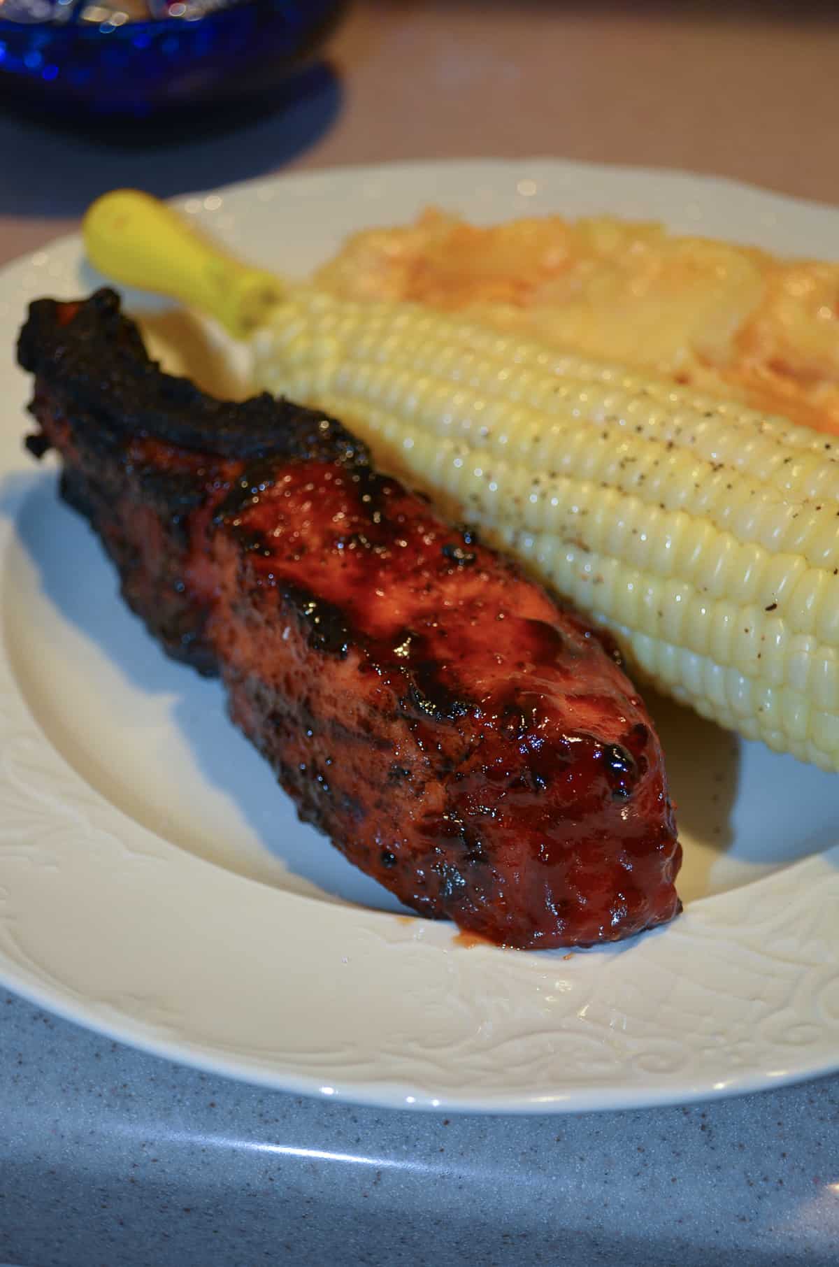A Grilled Country Style Rib on a white plate with corn on the cob.