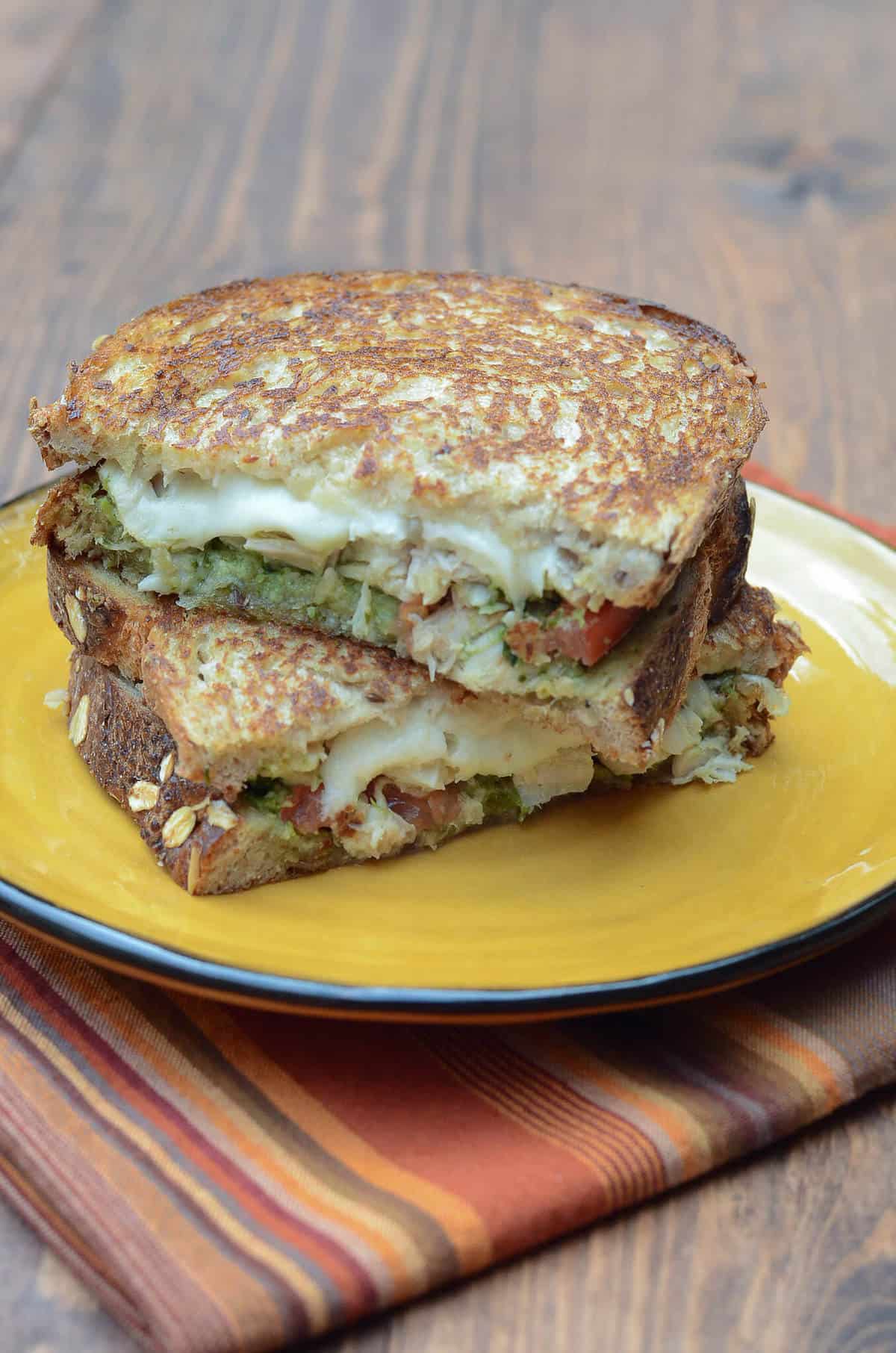 A Turkey Pesto Grilled Cheese Sandwich cut in half and stacked on a yellow plate.