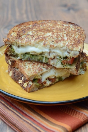 A turkey sandwich with pesto and cheese cut in half and stacked on a plate.