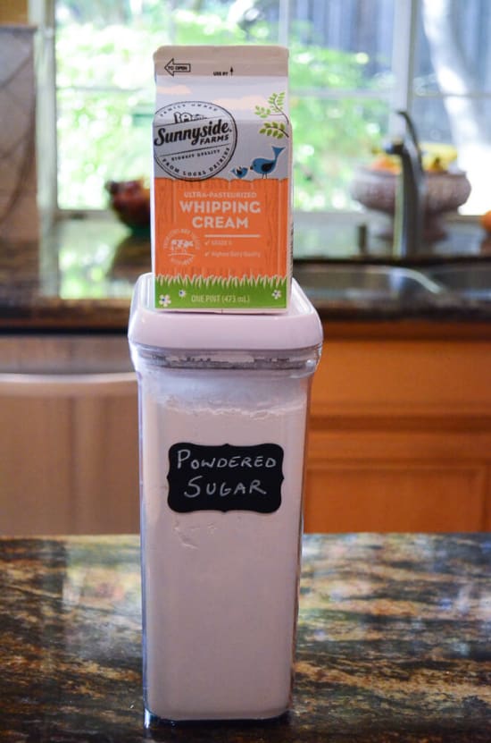 A container of whipping cream and powdered sugar on a kitchen counter.