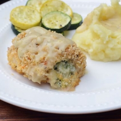 Breaded chicken stuffed with broccoli and cheese on a plate with mashed potatoes and vegetables.
