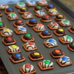 Square pretzels on a baking sheet topped with melted Kisses and M&M's.