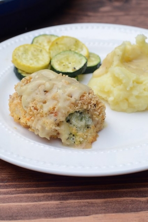Breaded chicken stuffed with broccoli and cheese on a plate with mashed potatoes and vegetables.