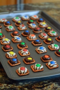 Square pretzels on a baking sheet topped with melted Kisses and M&M's.