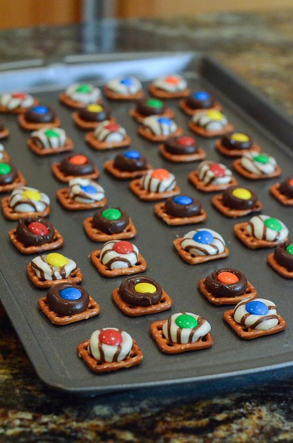 Square pretzels on a baking sheet topped with melted Kisses and M&M's.