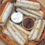 Rolled and baked tortillas on a platter with sour cream and salsa.