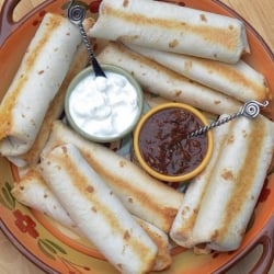Rolled and baked burritos on a plate with salsa and sour cream.