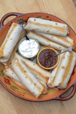 Rolled and baked burritos on a plate with salsa and sour cream.