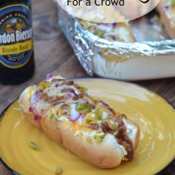 A yellow plate with a chili dog next to a beer.