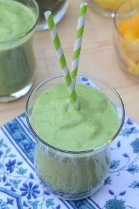 A green smoothie in a glass with two green and white straws.