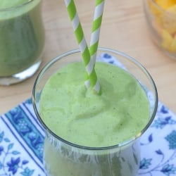A green smoothie in a glass with two green and white straws.