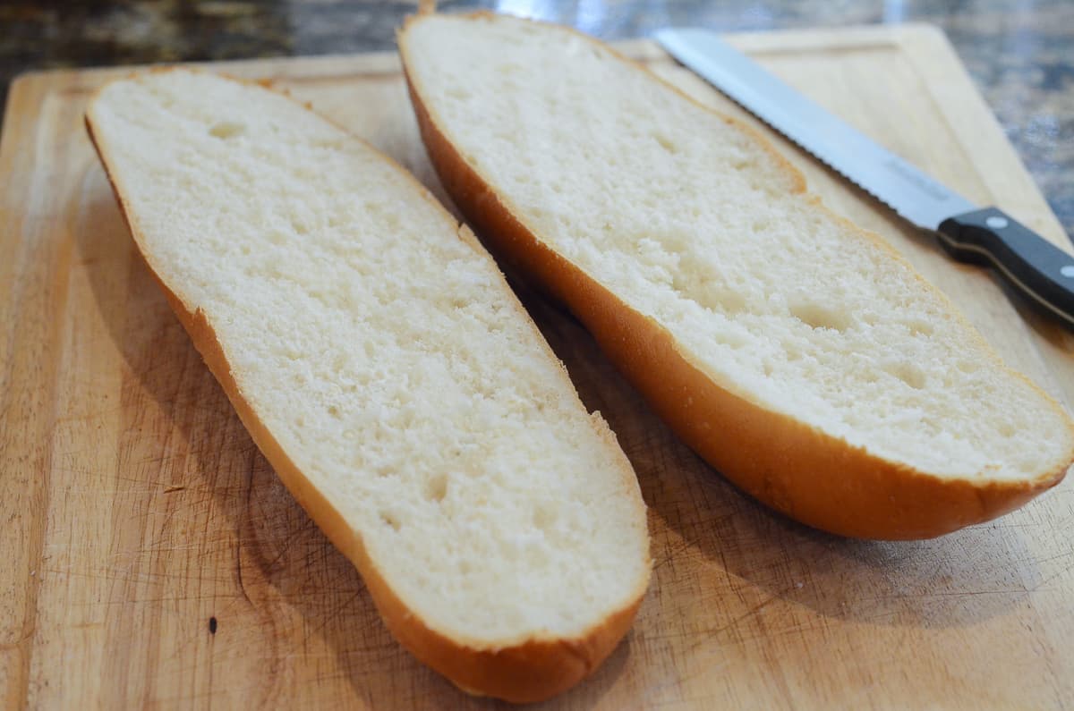 A loaf of French bread sliced in half on a cutting board.