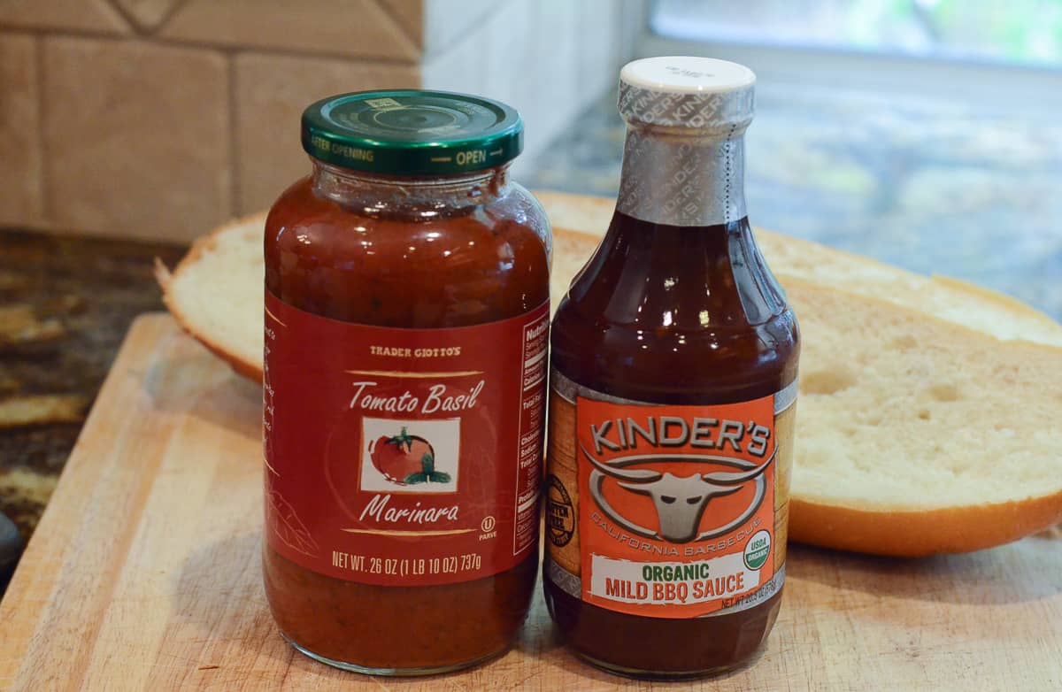 A jar of Trader Joe's Marinara and Kinder's BBQ Sauce on a kitchen counter.