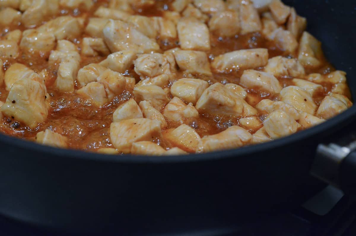 Pieces of chicken simmering in BBQ sauce in a skillet.