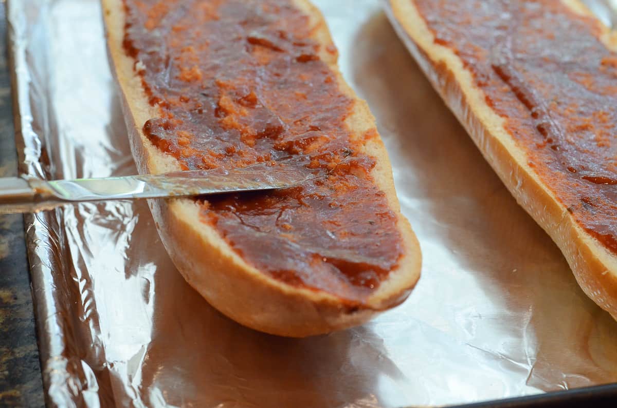 A knife spreading marinara sauce on French bread.