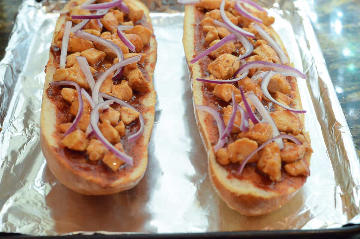 Sliced red onion on top of French bread pizza on a foil lined baking sheet.