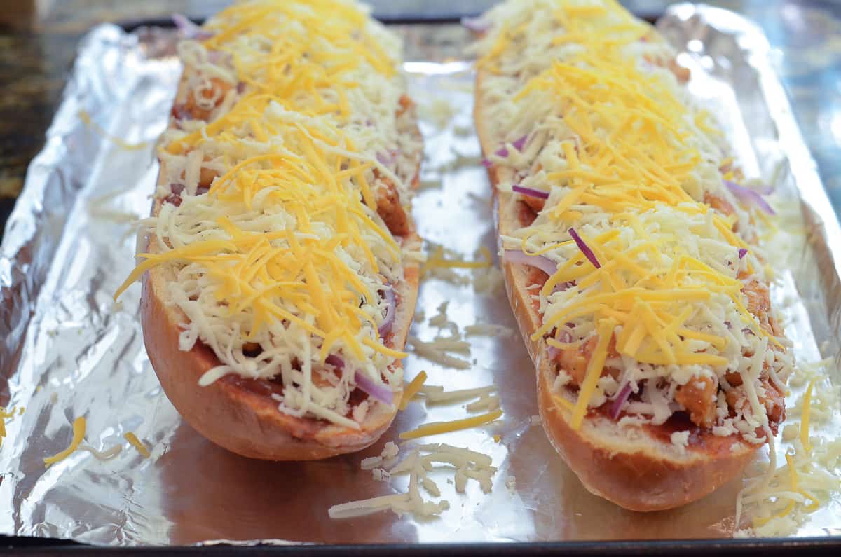 Shredded cheese on top of BBQ Chicken French Bread Pizza on a foil lined baking sheet.