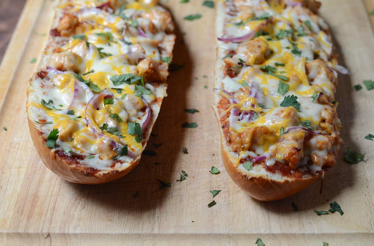 French bread pizza topped with cilantro on a cutting board.