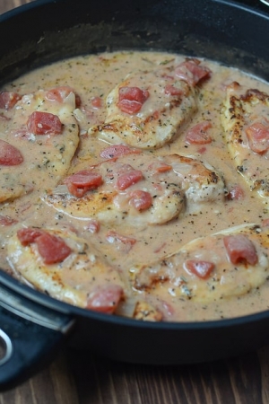 Chicken and sauce with tomatoes in a skillet.