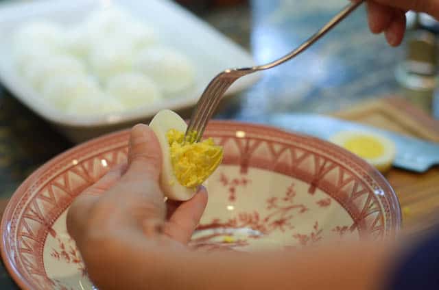 Removing the egg yolk from half of a hard boiled egg with a fork.