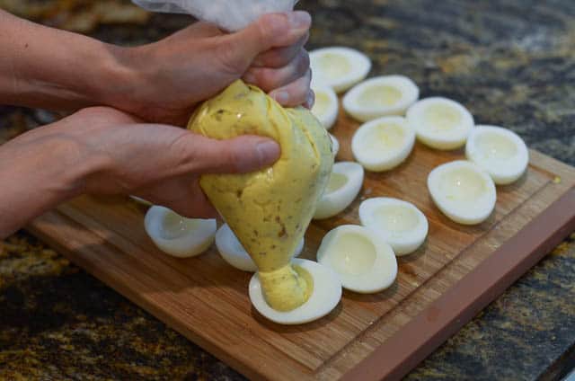 Using the plastic storage bag as a makeshift pastry bag to fill the empty egg whites.