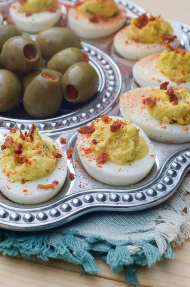Bacon Horseradish Deviled Eggs on a silver serving platter with green olives.