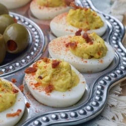 A metal egg tray filled with deviled eggs topped with crumbled bacon.