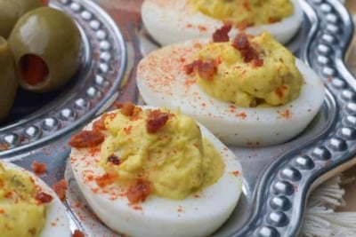 A metal egg tray filled with deviled eggs topped with crumbled bacon.