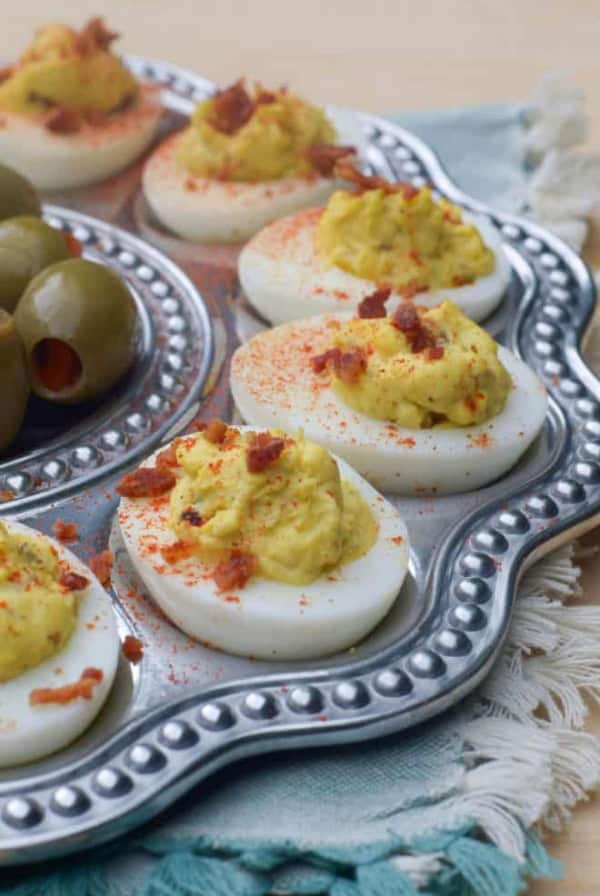 A metal egg tray filled with deviled eggs topped with crumbled bacon.