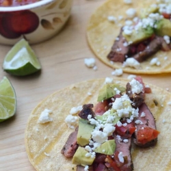 Corn tortillas topped with slices of steak, avocado, and crumbled cheese.