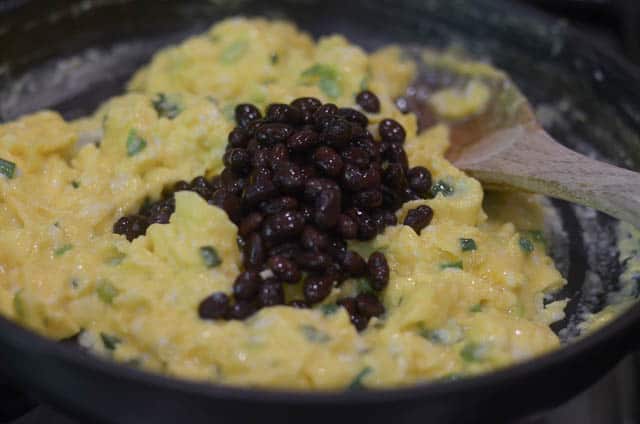Black beans being mixed into the egg mixture in the skillet.