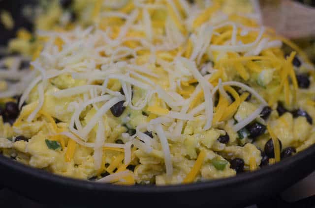 Shredded cheese being mixed into the cooked egg mixture.