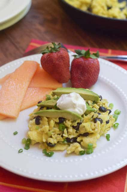 Mexican Scrambled Eggs on a white plate topped with avocado and sour cream with fruit.