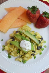 A plate of scrambled eggs with black beans, avocado, and sour cream.
