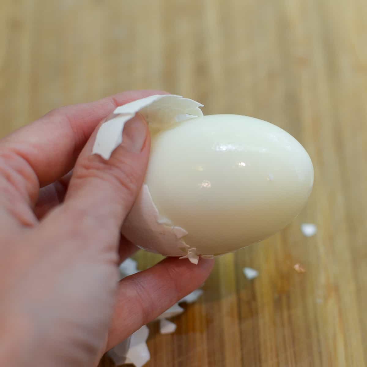A hand pulls the shell away from a hard boiled egg.
