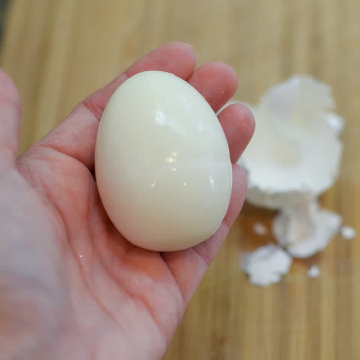 A hand holds a freshly peeled hard boiled egg.