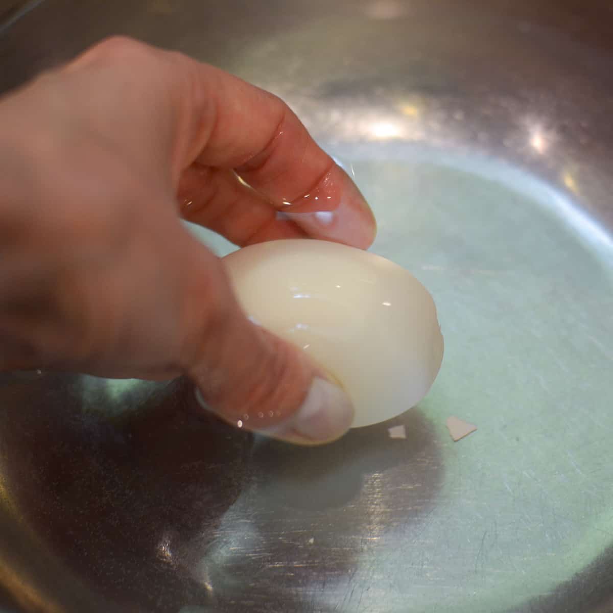 A hand dipping a peeled egg into a bowl of water.