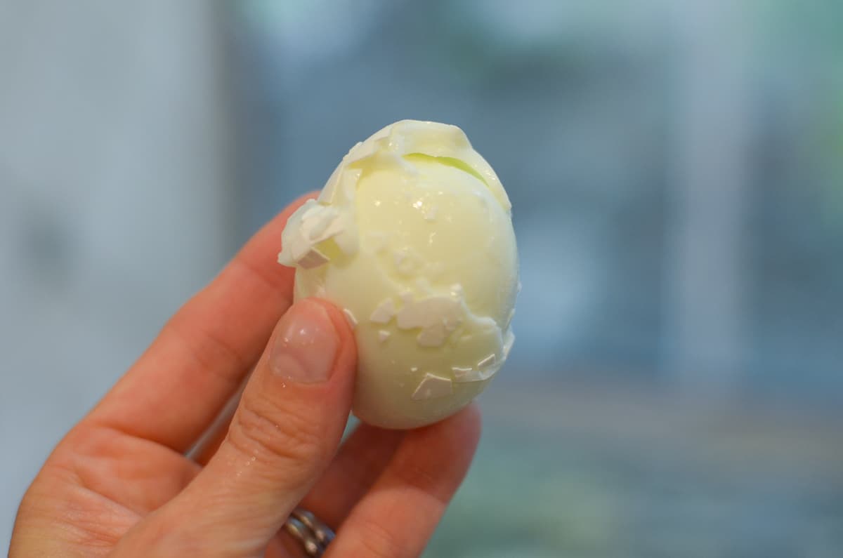 A hand holding a poorly peeled egg.