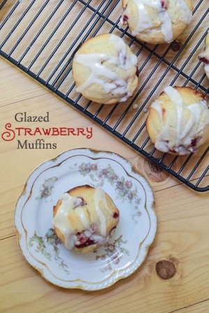 A glazed strawberry muffin on a china plate on top of a cutting board.