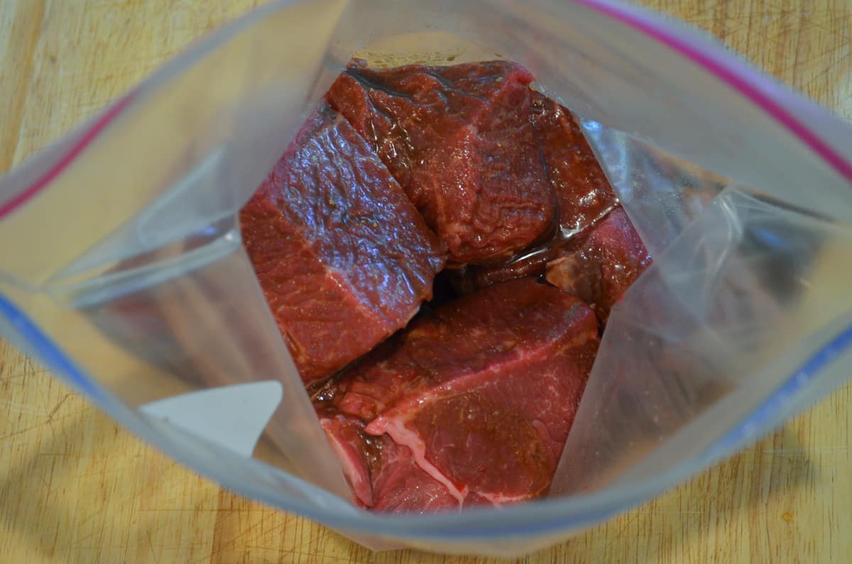 Chunks of steak in marinade in a plastic storage bag.