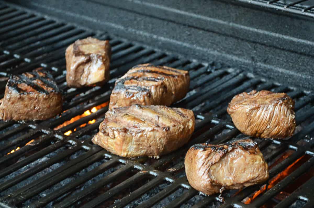 Pieces of steak cooking on a grill.