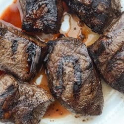 Grilled steak with juices on a white plate.