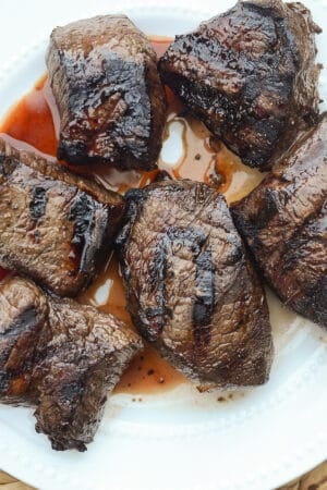 Grilled steak with juices on a white plate.
