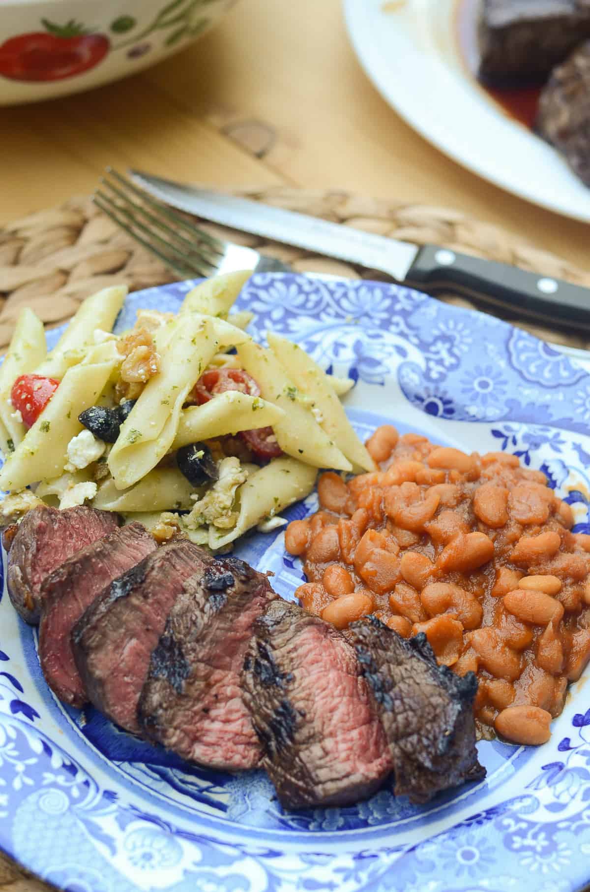 Sliced Whiskey Balsamic Steak on a blue plate with pasta and beans.