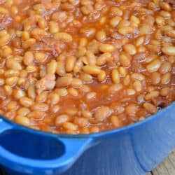 Baked beans in a blue pot on a wood board.