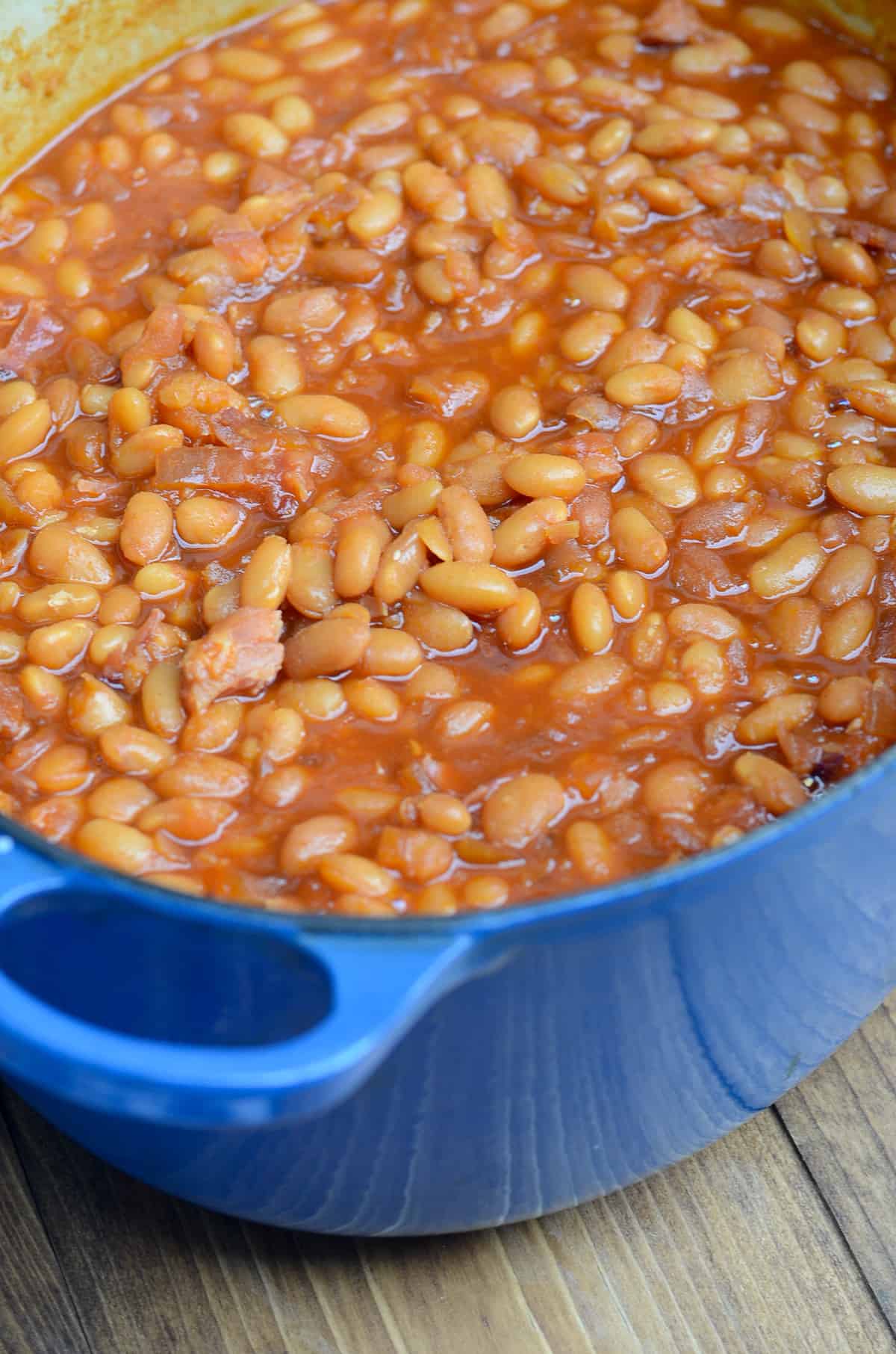 Baked beans in a blue pot on a wood board.