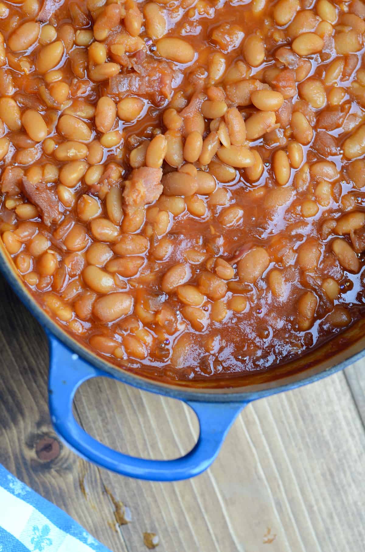 A top down shot of baked beans in a blue pot on a wood board.