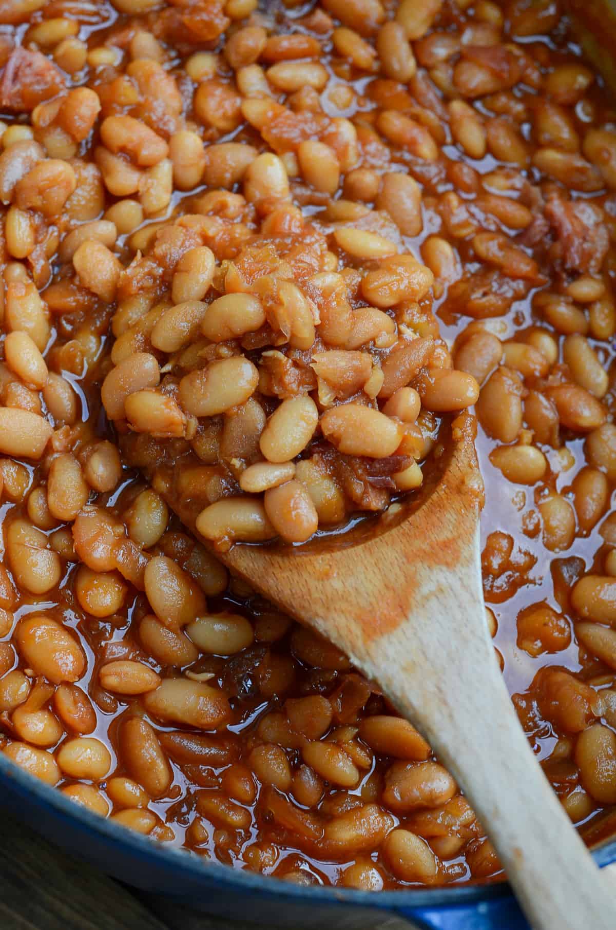 A close up of a wooden spoon scooping baked beans from a pot.
