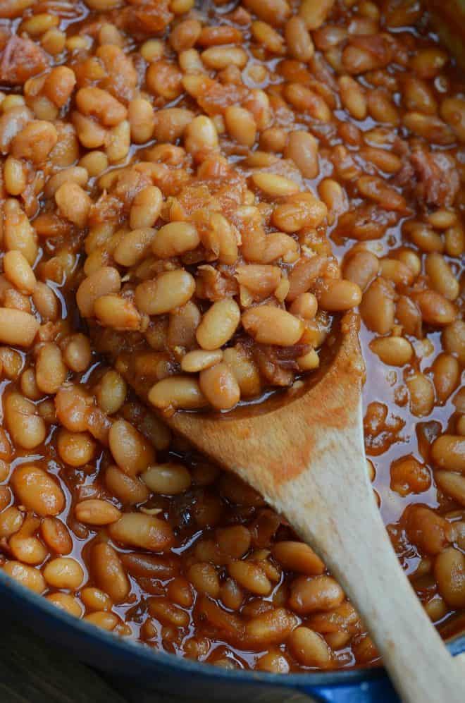 A close up image of a wooden spoon scooping up baked beans.